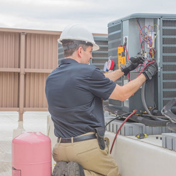 AC repair specialist cleaning the condenser coils of an outdoor unit with a pressurized air hose."