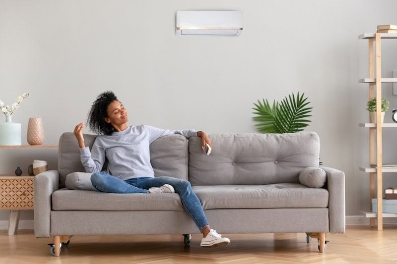 Female homeowner enjoying the cool breeze from her ductless mini split mounted to wall behind her.