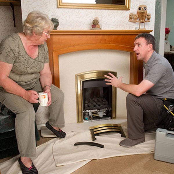 A tech and woman sitting on the floor near a fireplace during an installation process.