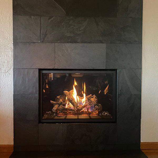 A cozy fireplace with a black stone wall, featuring a warm, flickering fire, highlighting a stylish installation.