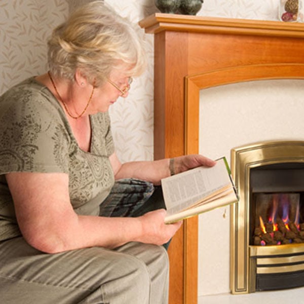A woman engrossed in a book, sitting by a gas fireplace that adds warmth and ambiance to the scene.
