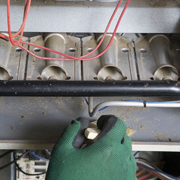 Technician Cleaning A Natural Gas Furnance A person in gloves works on a gas furnace installation, focusing on the equipment with a green glove on their hand.
