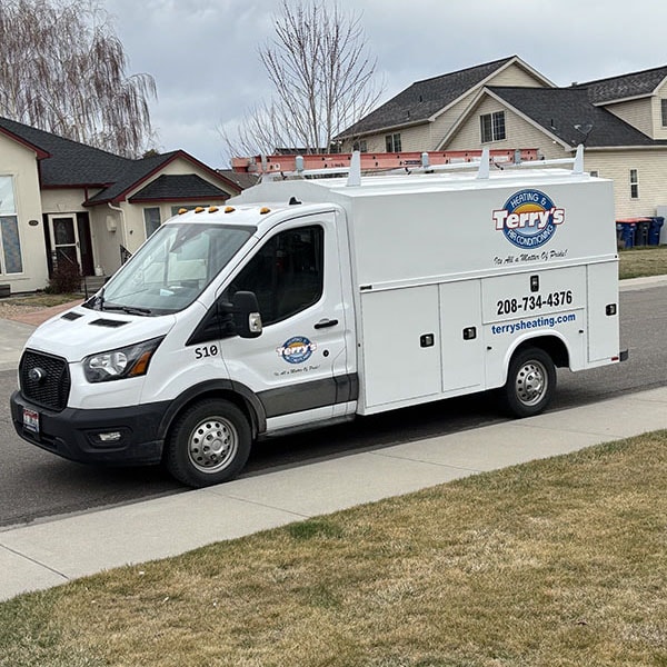 A white utility truck is parked outside a house, indicating a gas furnace repair service is on-site.