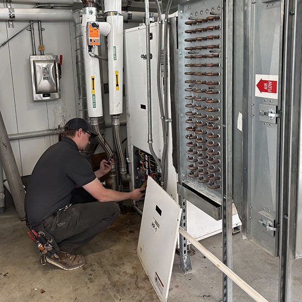 Gas-furnance-1_600x600 Employee working on electrical components inside an open panel of a large industrial HVAC unit in a mechanical room.