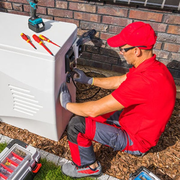 A technician wearing a red shirt and hat works on installing a heat pump for an air conditioning unit.