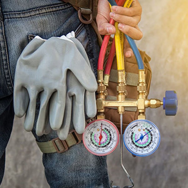A man holds a hose and two gauges, working on HVAC systems for new construction projects.