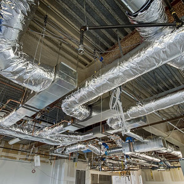 Interior of a spacious room with visible pipes and wires, showcasing HVAC new construction work.
