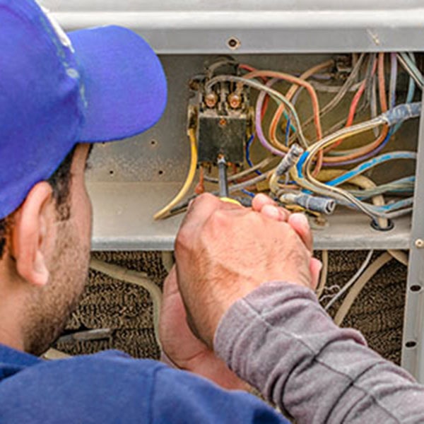 A man in a blue hat is working on an air conditioner, performing heat pump repairs.
