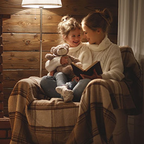 Two children sitting together in front of a cozy fireplace, with an oil furnace visible in the background.