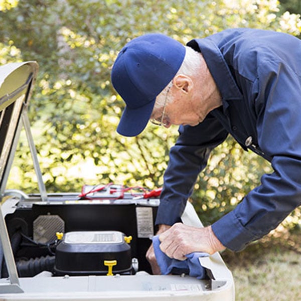 An oil-to-gas conversion technician in blue overalls is fixing an air conditioner, adjusting its internal mechanisms.