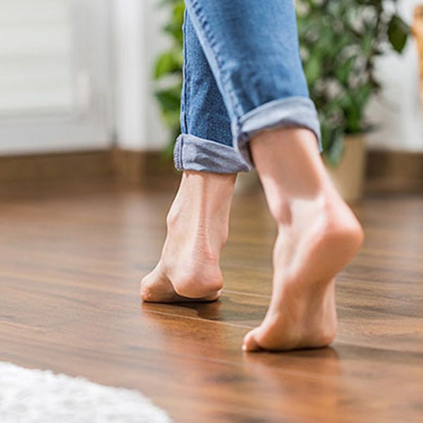 A woman's feet in motion on a wooden floor, illustrating the cozy effect of radiant floor heating underneath.