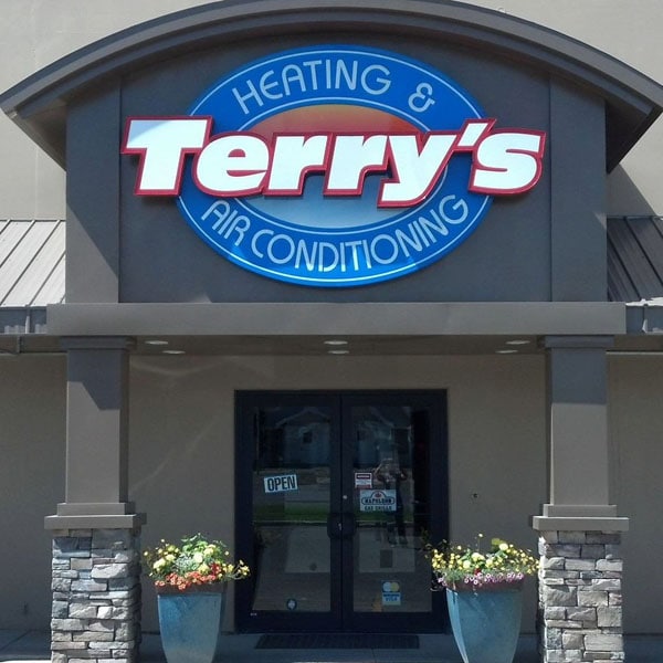 Front entrance of Terry’s Heating & Air Conditioning building, featuring a large blue and red sign above double glass doors with 'OPEN' sign and flower pots on each side.