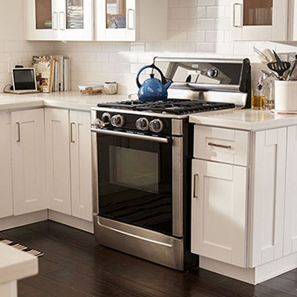 Bright kitchen with white cabinets, dark wood floor, and a stainless steel stove. A blue kettle sits on the stove, adding a cozy touch.