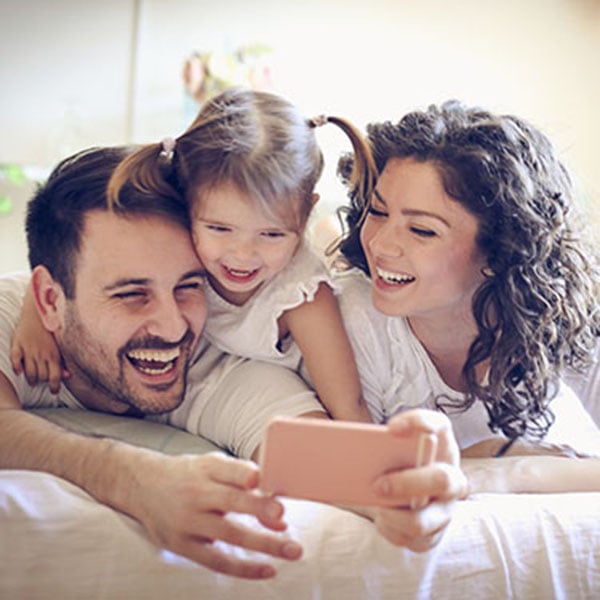 Tankless Water Heaters 1_600x600 A man, woman, and child on a bed smiling for a selfie, showcasing a cozy family moment.