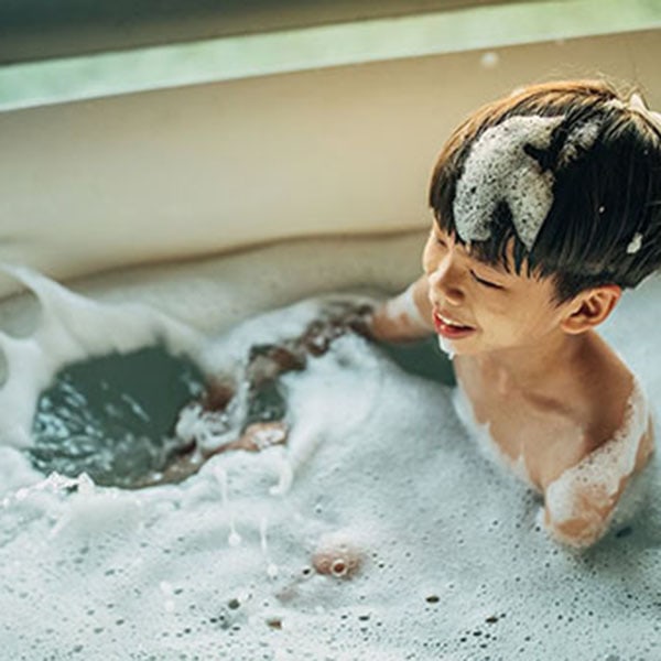 A young boy is happily bathing in a spacious tub, with water splashing around him in a bright bathroom.