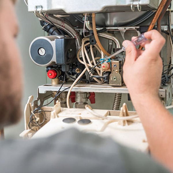 A technician is working on a gas furnace, adjusting components for proper functionality and safety.